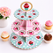 Three-tiered cupcake stand with polka dot and striped design, surrounded by cupcakes on a white background.